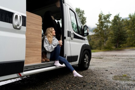 Frau sitzt vor weißem Miet-Camper 2025