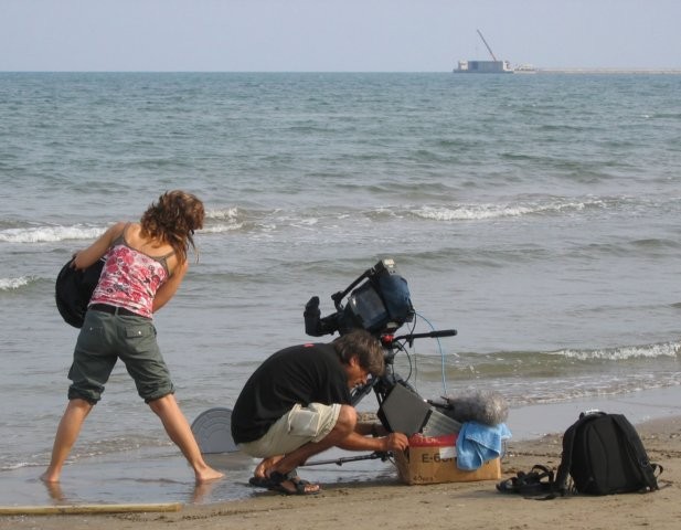 Hier wordt een kunstzinnig videoclipje opgenomen: De zee, het strand en een doos van een filmspoel.