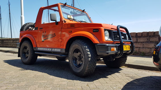 Oranje Suzuki Samurai geparkeerd langs de haven muur in West Terschelling
