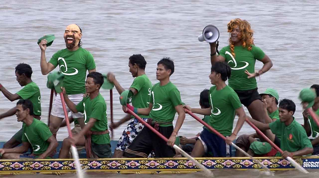   Bouffons engagés sur une pirogue de course durant la fête de l'eau en 2016 à Phnom Penh. © Patrick Kersalé 2016-2024.