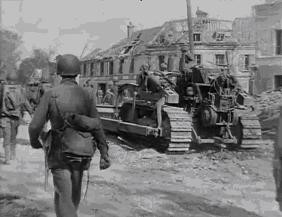Crossroads of D13 and D16, center of Chambois. A bulldozer (unknown tool to the French) moving debris. Americans probably from 358 or 359 Regt (90 US ID). Frame from movie Death and Destruction in the Falaise Gap.