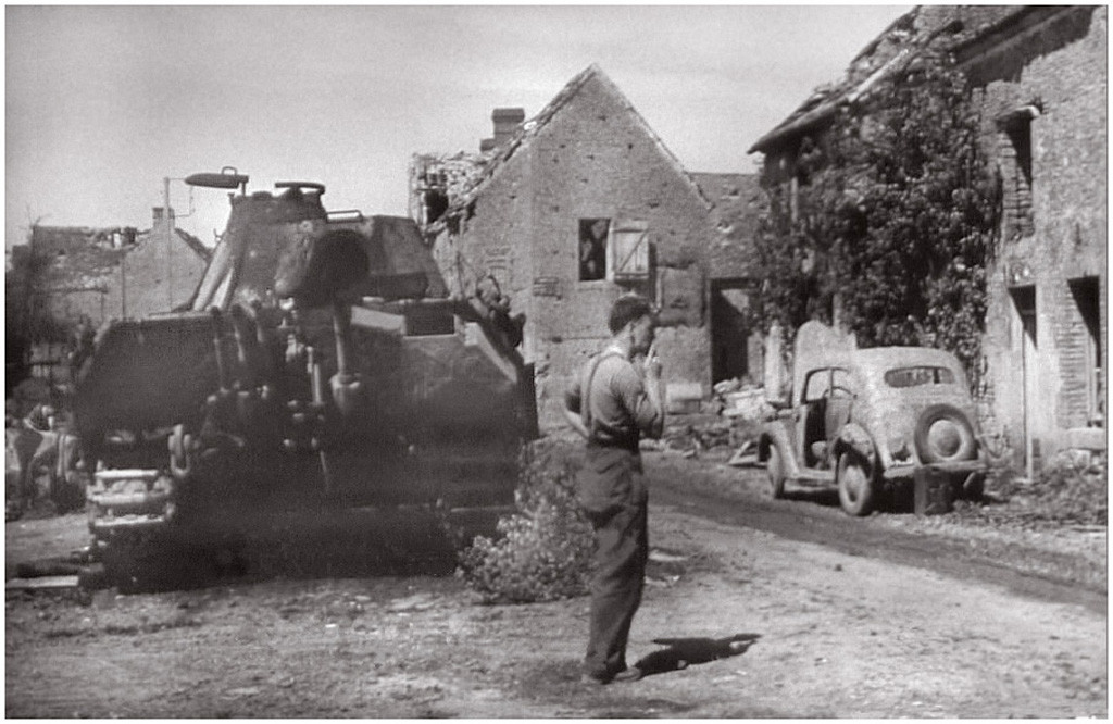 A soldier (at least looking to be) standing next to a Panther put out of service. On the right side of the road there is an Opel Olympia: http://www.o5m6.de/opel_olympia.html