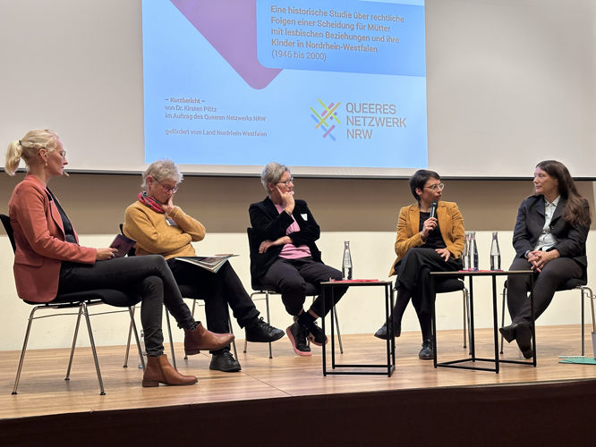 Eine Podiumsdiskussion mit fünf Frauen auf der Bühne, präsentiert vom Queeren Netzwerk NRW.