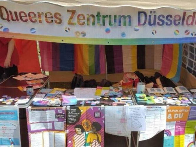 Infostand des Queeren Zentrums Düsseldorf auf dem CSD-Straßenfest 2025 mit Banner, Flyern und Plakaten