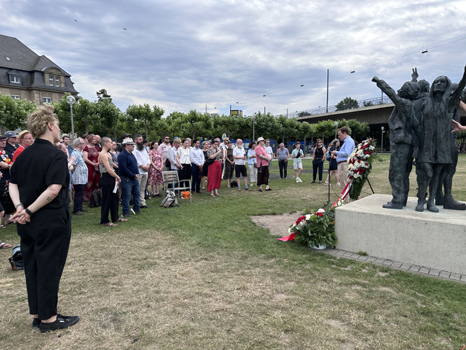 Gruppe von Menschen bei Gedenkveranstaltung vor Denkmal mit Bronzestatuen