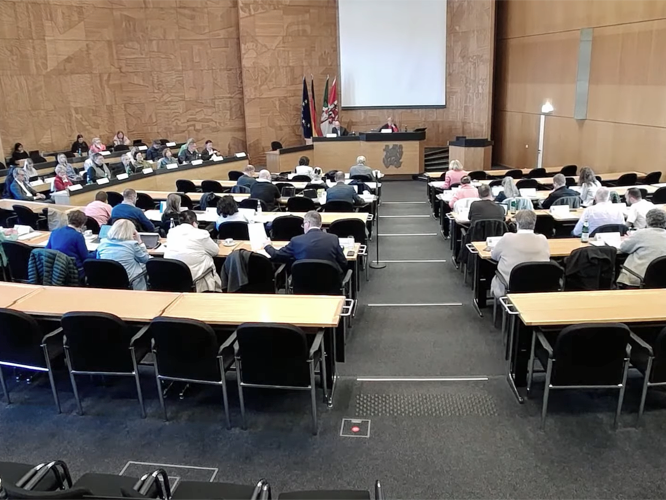 Blick in den Plenarsaal des Düsseldorfer Rathauses mit sitzenden Menschen an Tischreihen.