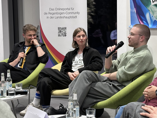 Drei Personen sitzen auf grünen Sesseln bei einer Podiumsdiskussion.