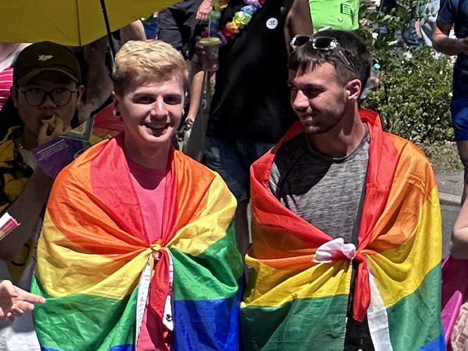 Demo-Teilnehmende gehüllt in Regenbogenfahnen