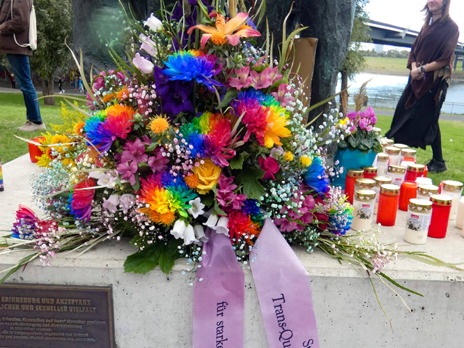 Bild: Buntes Blumengesteck mit Gedenkschleifen am LSBTIQ+ Denkmal