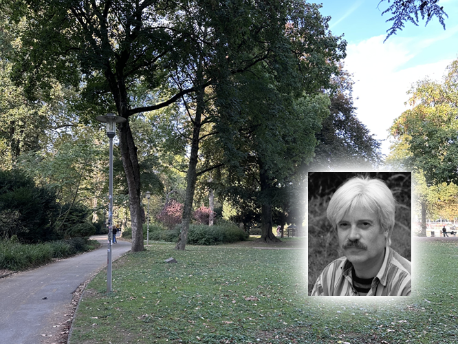 Ein gepflegter Weg in einem parkähnlichen Gelände mit Bäumen und Grünflächen; im Vordergrund ein überlagerter Ausschnitt mit dem Porträtfoto eines Mannes mit hellem Haar und Mustache.