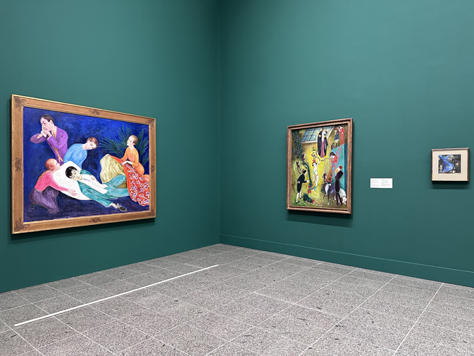 Ausstellungsraum mit drei gerahmten Gemälden an einer türkisfarbenen Wand: Links ein großes Bild mit farbenfrohen Figuren, in der Mitte ein weiteres farbenreiches Gemälde, und rechts ein kleines Bild.