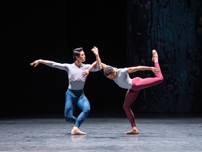 Zwei Balletttänzer. Einer mit blauer Hose, der andere mit roter Hose. Miteinander tanzend.