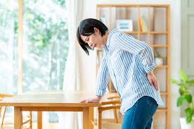 長時間のデスクワークで腰に疲れを感じている人のイラスト｜身体の不調とメンタルのつながり（世田谷心理カウンセリングルーム）