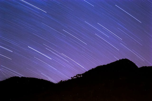 Paisagem de montanhas mostrando estrelas cadentes no céu durante a noite