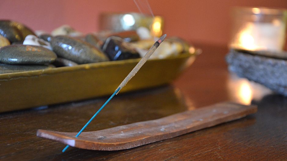 Hölzerner, flacher Räucherstäbchenhalter, in dem ein glimmendes Räucherstäbchen steckt