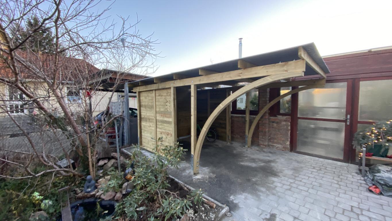 Holzcarport mit zwei geschwungenen Stützbögen und integriertem Geräteraum, fachgerecht montiert in Dresden mit Trapezblechdach.