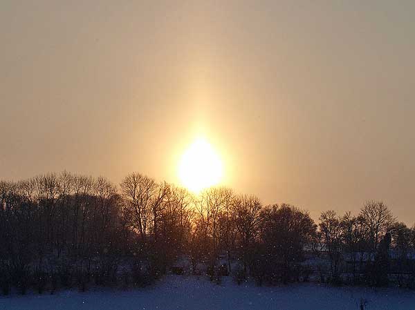 Morgensonne wie eine brennende Kerze, Sonnenaufgang über Schnee mit Schneefall in St. Johann, Schwäbische Alb