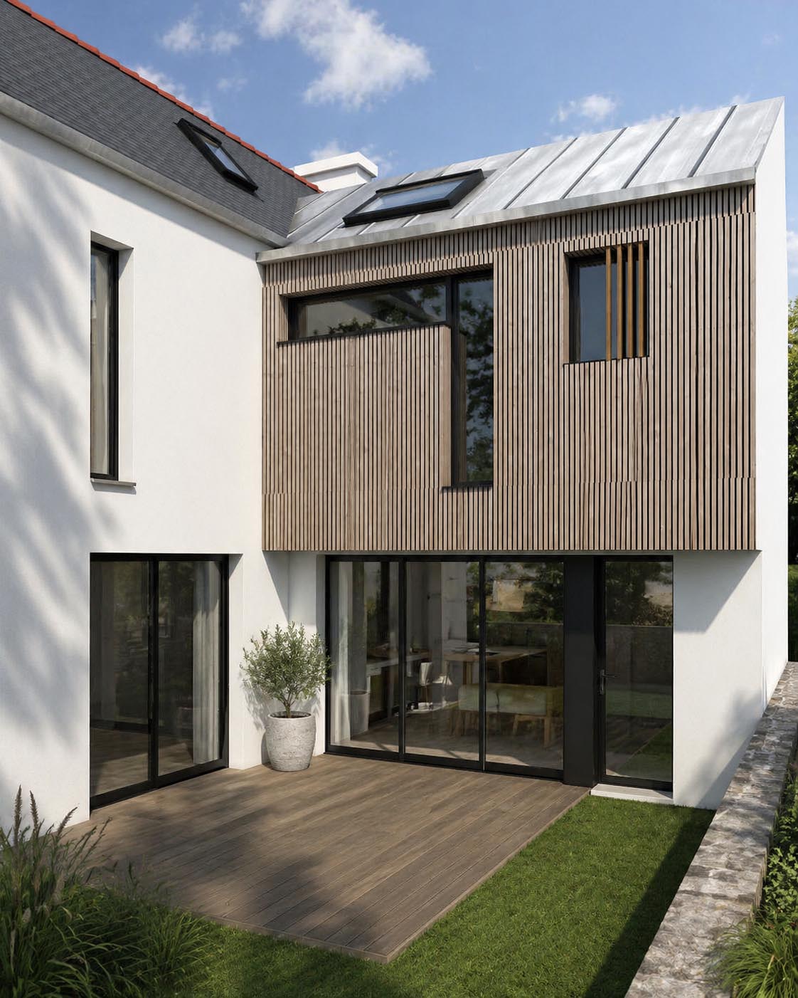 Extension contemporaine de maison avec bardage bois, toiture zinc, grandes baies vitrées et terrasse extérieure.