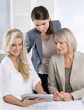 Im Bild sind 3 Frauen - 2 sitzen, sind blond, 1 steht, dunkelhaarig - alle 3 betrachten etwas auf einem Tablet.