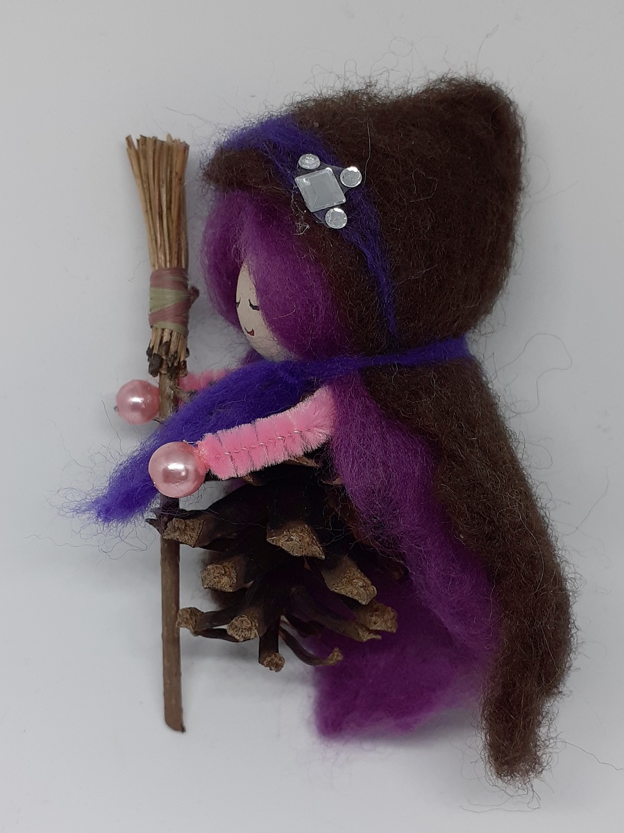 Hexe Viola Seitenansicht. Handgefertigte Hexenfigur aus Kiefernzapfen, mit violetten langen Haaren und nadelgefilztem braunen Hexenmantel aus Wolle, silberne Ziersteinen, Hexenbesen aus Kiefernnadeln