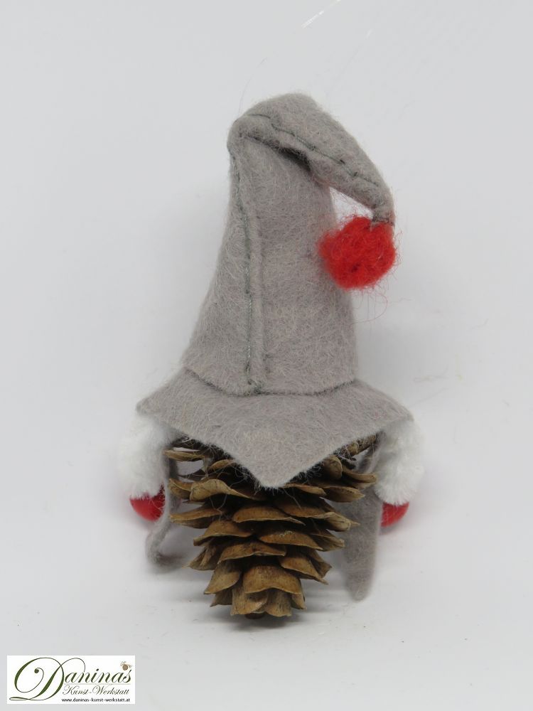 Wichtel Treuherz, Rückseite. Handgemachte Märchenfigur aus Lärchenzapfen, graue Filz Jacke und Mütze mit roten Herzen und einem roten Bommel.