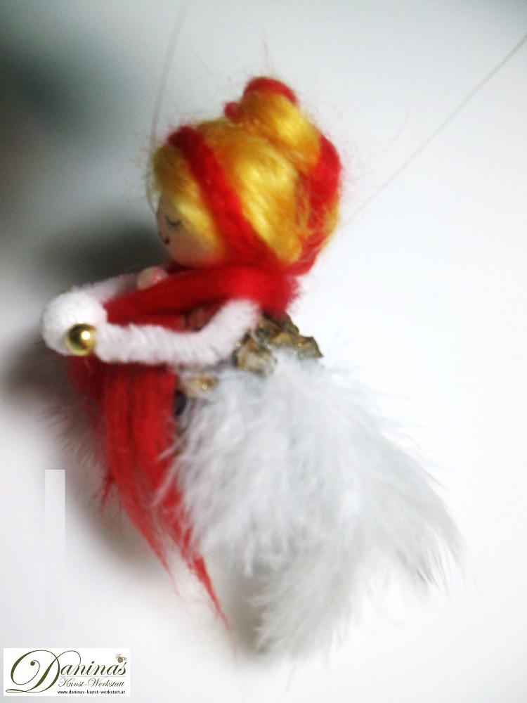 Winterfee Figur Schneeflocke Seitenansicht, handgefertigt aus Kiefernzapfen, mit goldenen Haaren und rotem Schal aus Wolle, weißen Federnflügeln und einem Schneeball.