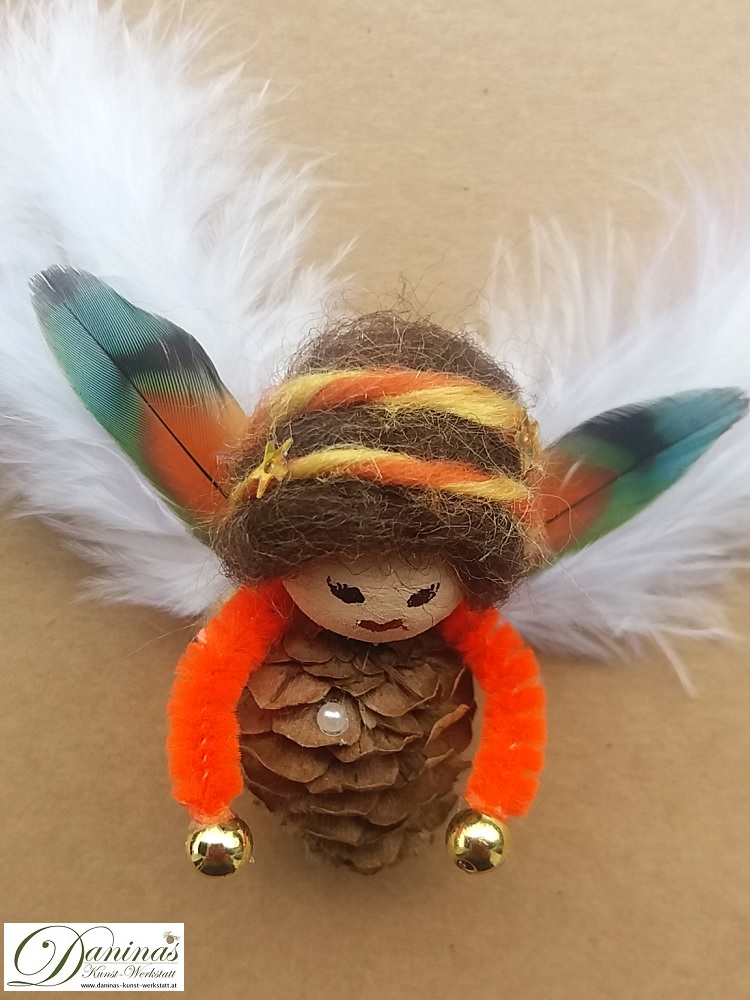 Schutzengel Figur Peachy aus Lärchenzapfen mit braunen Haaren und buntem Haarband aus Wolle sowie bunten und weißen Federnflügeln.
