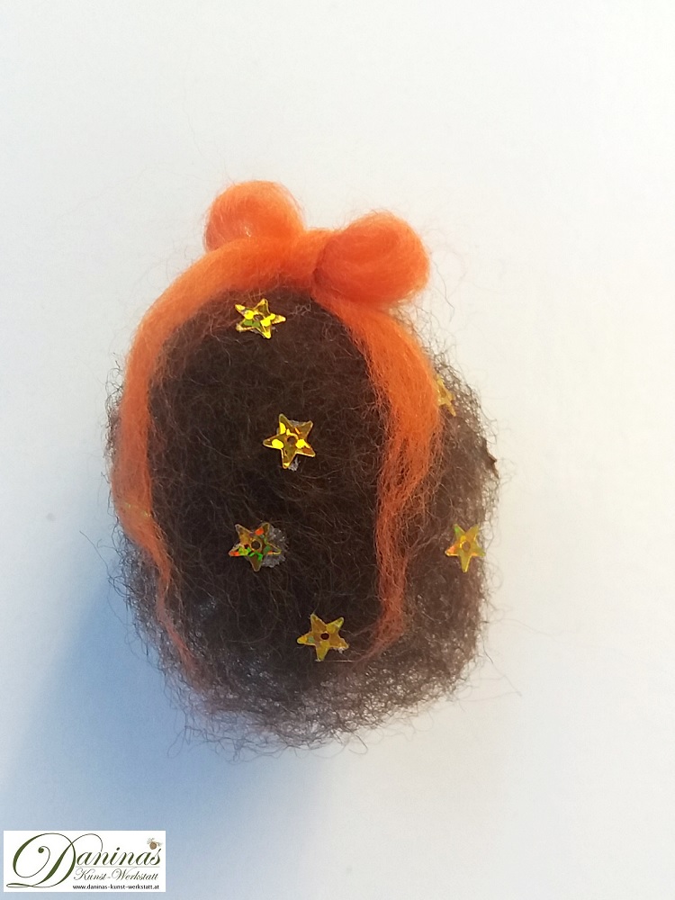 Kleine Hexe Stella, Rückseite. Handgefertigte Hexenfigur aus Kiefernzapfen, mit braunen langen Haaren aus Wolle mit Sternen und einem orangen Haarband, grüne und orange Bommeln im Zapfen