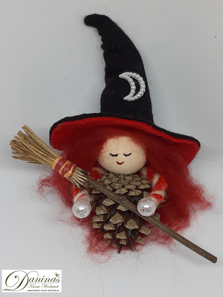 Hexe Astra. Handgefertigte Märchenfigur aus Kiefernzapfen, mit rostbraunen langen Haaren aus Wolle, einem schwarz-orangen Hexenhut aus Filz mit Perlenmond und einem Hexenbesen aus Kiefernnadeln