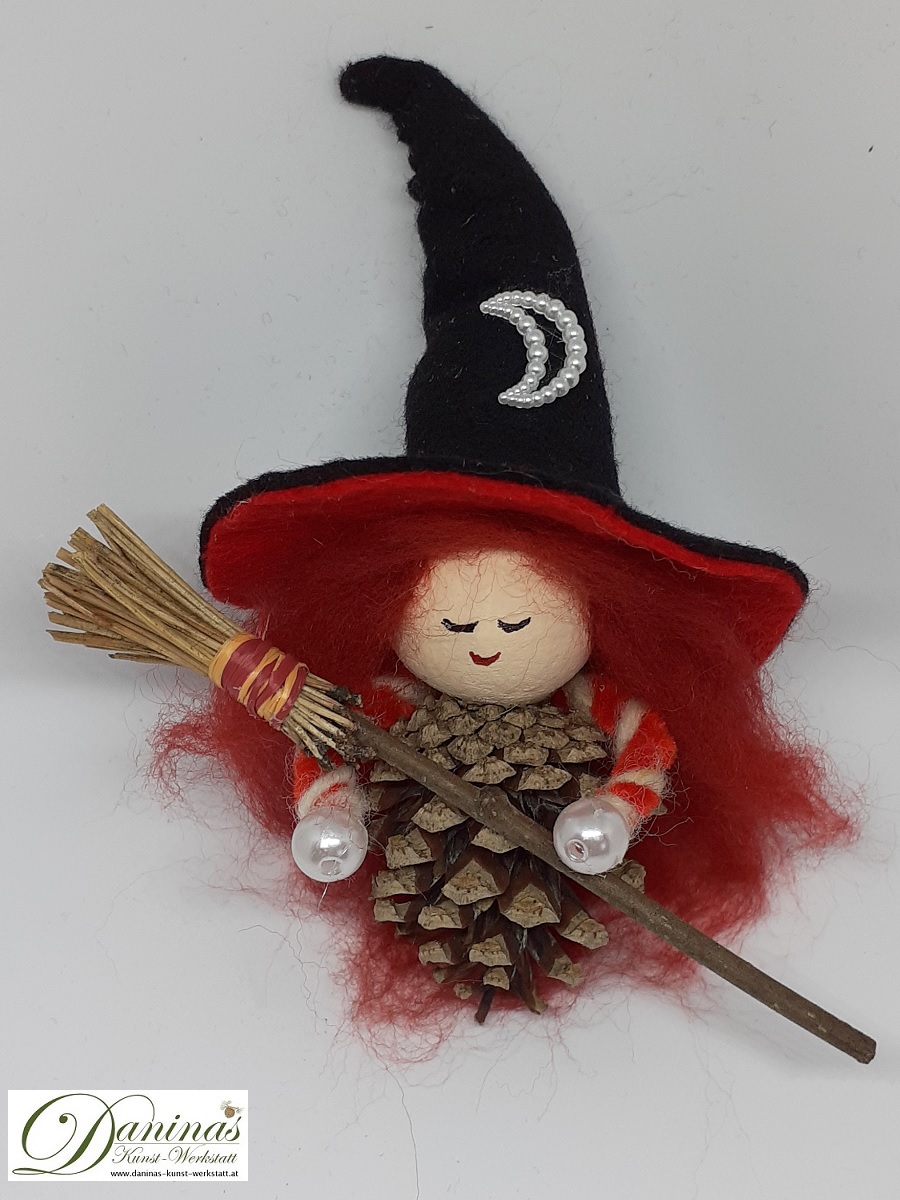 Hexe Astra. Handgefertigte Märchenfigur aus Kiefernzapfen, mit rostbraunen langen Haaren aus Wolle, einem schwarz-orangen Hexenhut aus Filz mit Perlenmond und einem Hexenbesen aus Kiefernnadeln