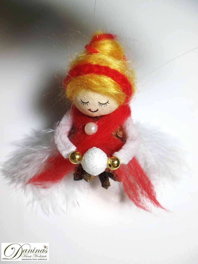 Winterfee Figur Schneeflocke aus Kiefernzapfen, mit goldenen Haaren und rotem Schal aus Wolle, weißen Federnflügeln und einem Schneeball.