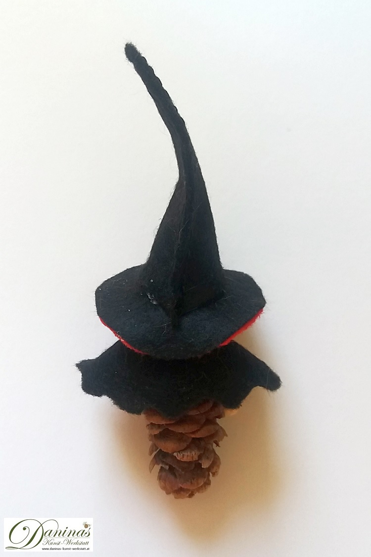 Hexe Wallburga, Rückseite. Handgefertigte Figur aus Douglasienzapfen, mit einem schwarz-roten Filz Jäckchen und einem Hexenhut mit roten Bommeln