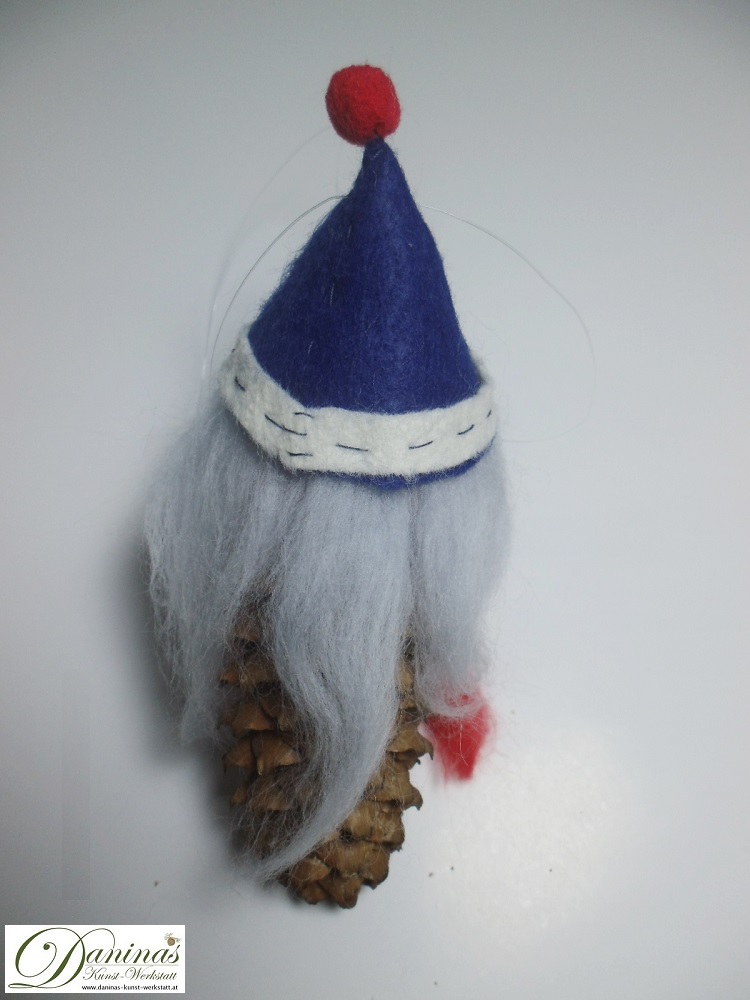 Winterfee Figur Lauriel Rückseite. Handgefertigt aus Fichtenzapfen, mit hellblauen langen Haaren und einem roten Schal aus Wolle sowie einer dunkelblauen Filzmütze.