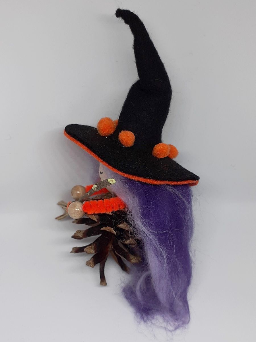 Hexe Holunda Seitenansicht. Handgefertigte Hexenfigur aus Kiefernzapfen, mit violett-lila langen Haaren aus Wolle und schwarz-orangem Hexenhut aus Filz, Hexenbesen aus Kiefernnadeln