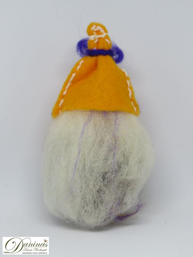 Hexe Strelitzia, Rückseite. Handgefertigte Hexenfigur aus Kiefernzapfen, mit weißen langen Haaren und einem orange-blauen Schal aus Wolle sowie einem orangen Filz-Hut mit blauem Band.