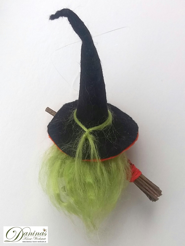 Hexe Hella, Rückseite. Handgefertigte Hexenfigur aus Kiefernzapfen, mit grünen langen Haaren aus Wolle, einem schwarz-orangen Hexenhut aus Filz mit einem magischen grünen Stein und einem Hexenbesen aus Zweigen