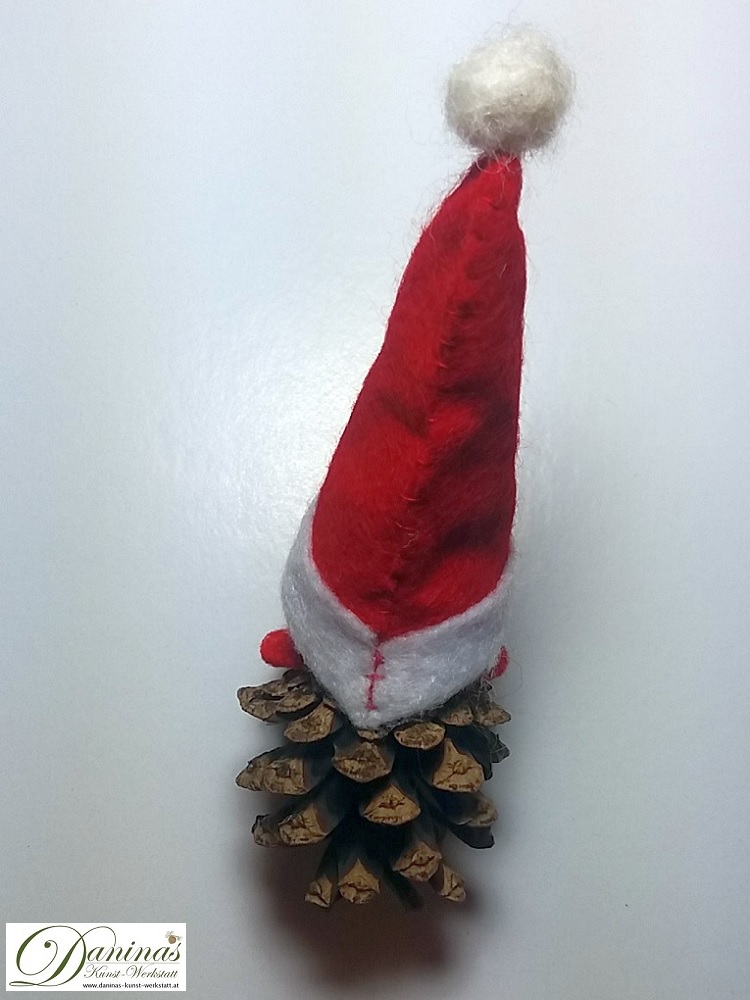 Weihnachtswichtel Bringfreud, Rückseite. Handgemachte Wichtelfigur aus Kiefernzapfen, mit braunen Haaren aus Wolle, rot-weißer Zipfelmütze  und weißem Schal aus Filz