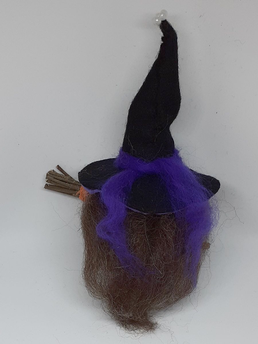 Hexe Lupinia Rückseite. Handgefertigte Märchenfigur aus Kiefernzapfen, mit braunen langen Haaren aus Wolle, schwarz-violettem Hexenhut aus Filz und Hexenbesen aus Zweigen