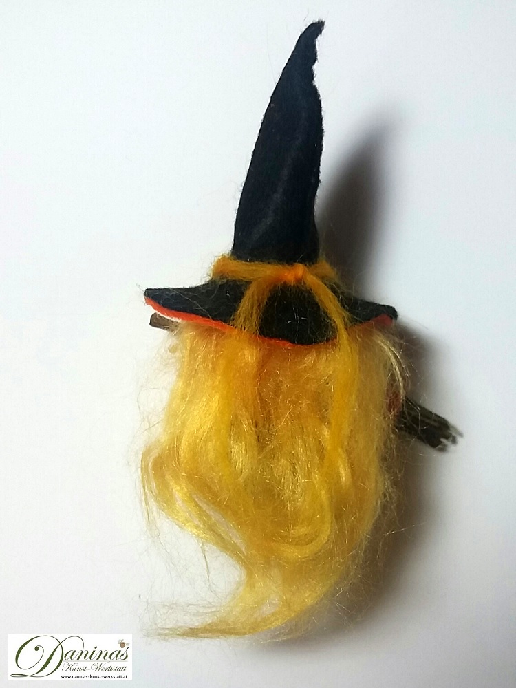 Hexe Kala, Rückseite. Handgefertigte Hexenfigur aus Kiefernzapfen, mit blonden langen Haaren aus Wolle, einem schwarz-orangen Hexenhut aus Filz und einem Hexenbesen aus Zweigen