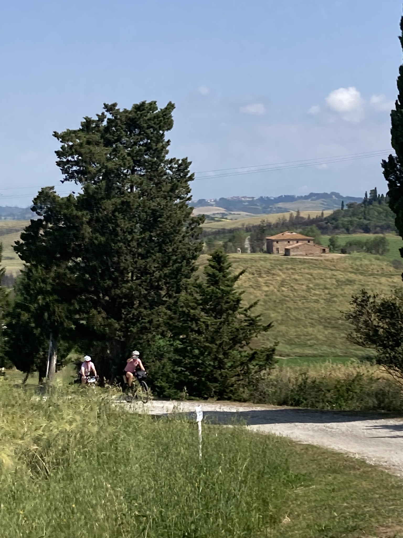 Bikepacking Italien - von Livorno nach Rimini: Zwei Radfahrer auf Schotterweg bei Lajatico, Zypressen und toskanische Hügellandschaft im Hintergrund, sonniges Wetter.