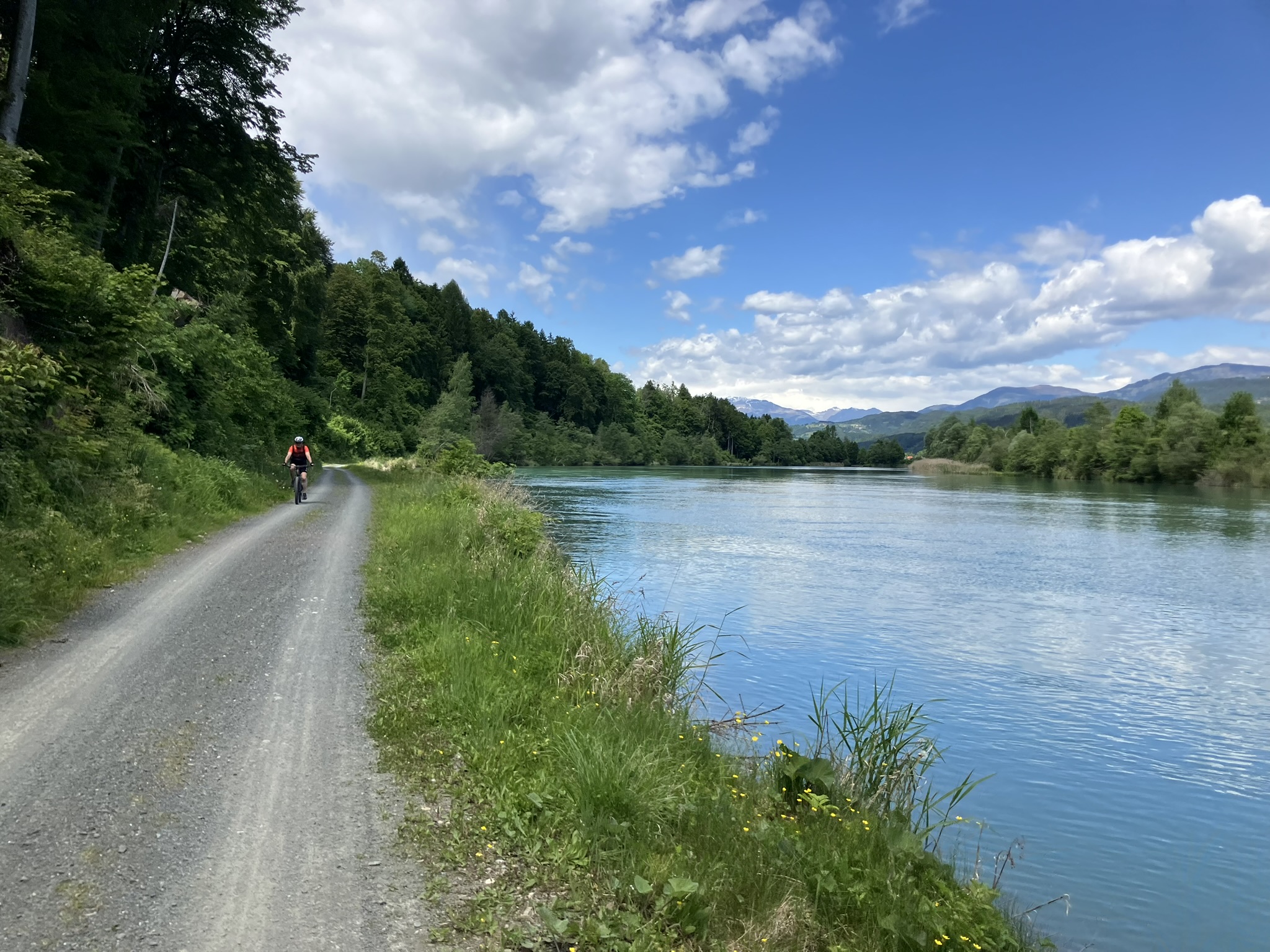 Gravel Bikepacking am Flussufer der Drau in Kärnten mit Wald, Bergen und Schotterweg direkt am Wasser.