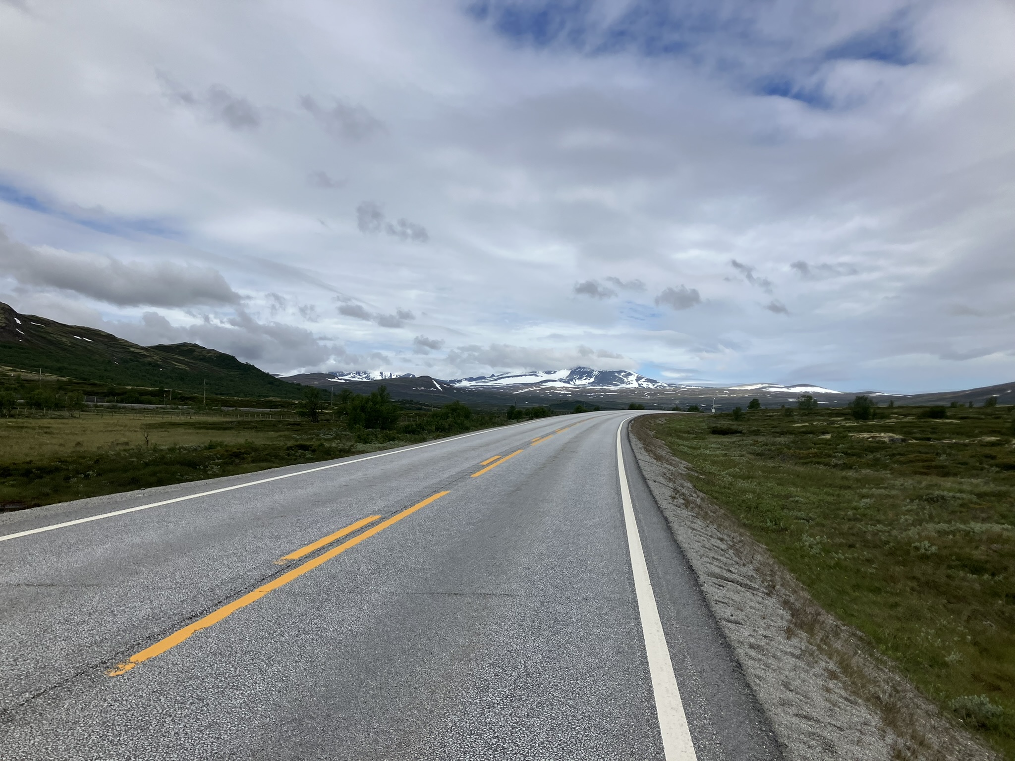 Bikepacking Schweden - Geführte Bikepacking-Tour von Stockholm nach Trondheim auf einsamer Straße durch die skandinavische Hochebene mit Blick auf schneebedeckte Berge.