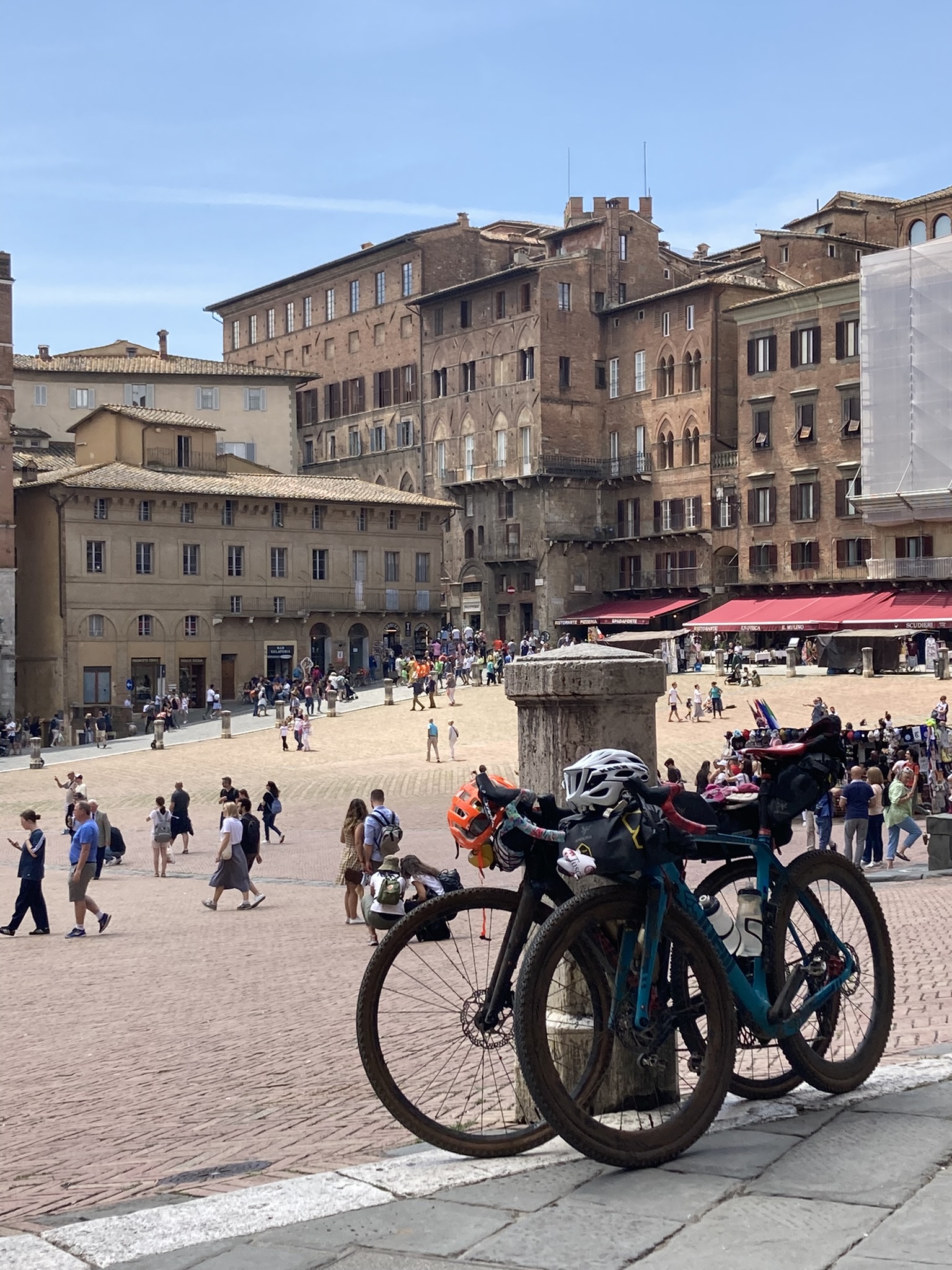 Bikepacking Italien - Gravel in der Toskana: beladenes Gravelbike auf der Piazza del Campo in Siena, historische Backsteinfassaden und lebendige Altstadt im Hintergrund.