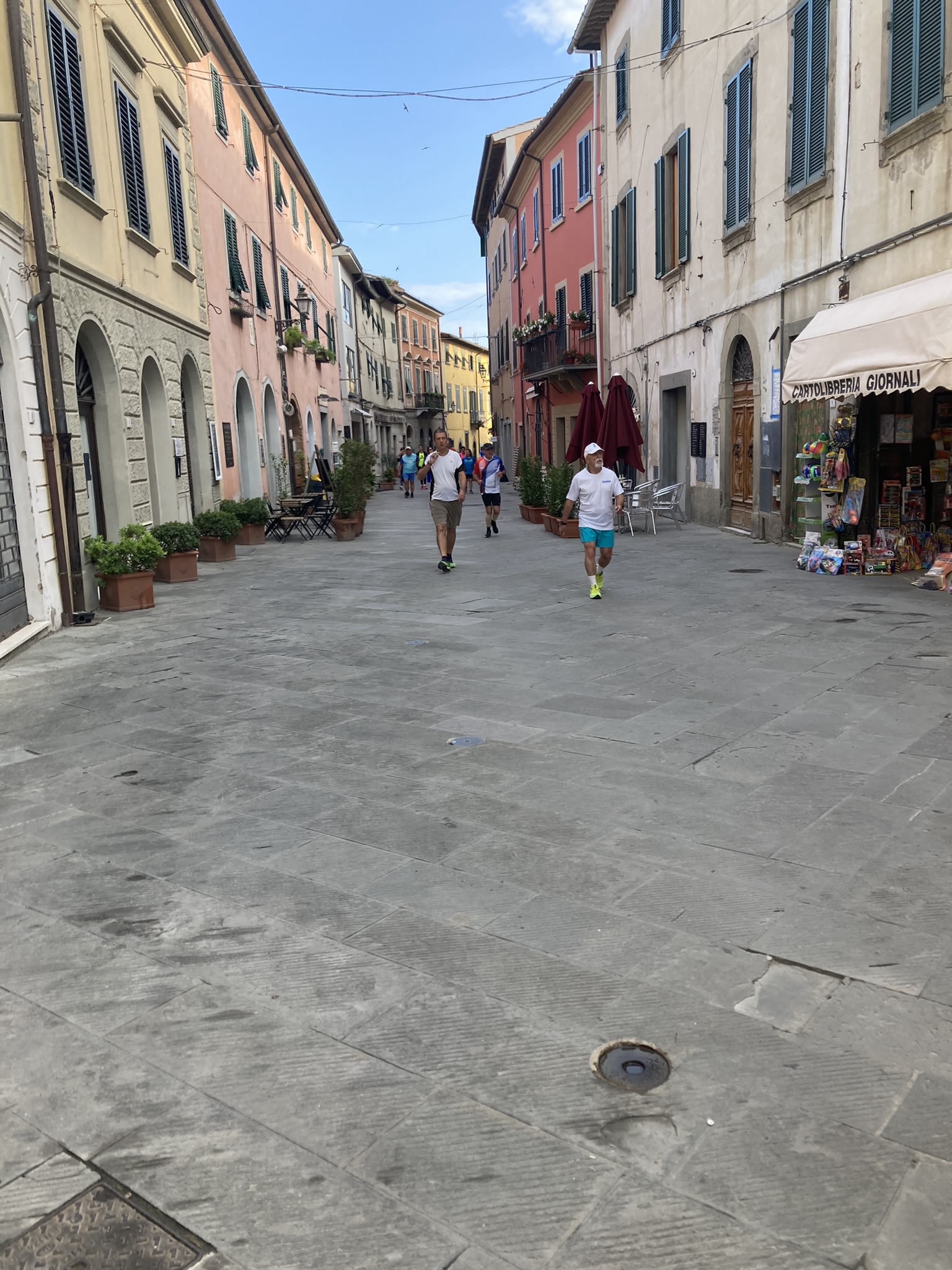 Bikepacking Italien - Toskana, historische Altstadtgasse mit pastellfarbenen Häusern und Fußgängern, aufgenommen während einer Gravel-Bikepacking-Etappe in Italien.