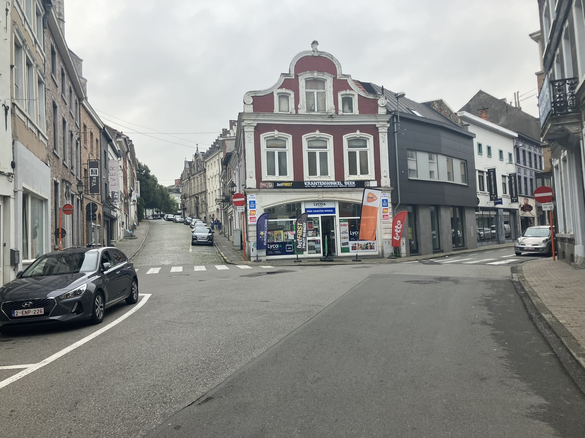 Bikepacking Belgien - Straßenszene in Tienen in Belgien mit historischen Gebäuden, Geschäft an einer Kreuzung und leicht bewölktem Himmel.
