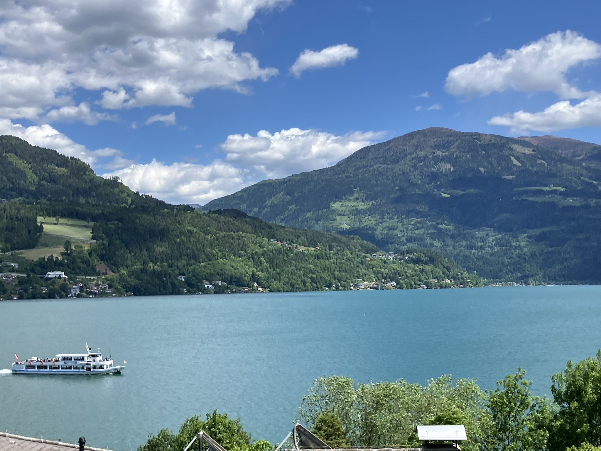 Bikepacking-Tour durch Kärnten – Millstätter See, Österreich – türkisblauer Alpensee mit Ausflugsschiff vor bewaldeten Berghängen unter sommerlichem Himmel.