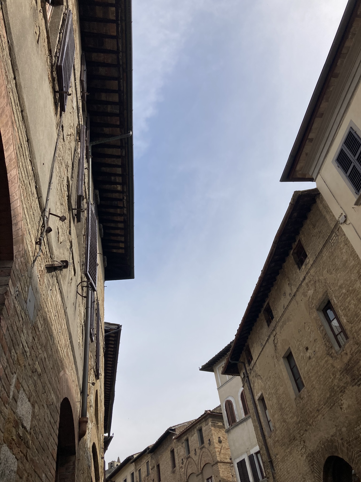 Bikepacking Italien - Toskana, schmale Altstadtgasse mit historischen Steinfassaden und Blick in den Himmel, aufgenommen während einer Gravel-Bikepacking-Etappe in Italien.