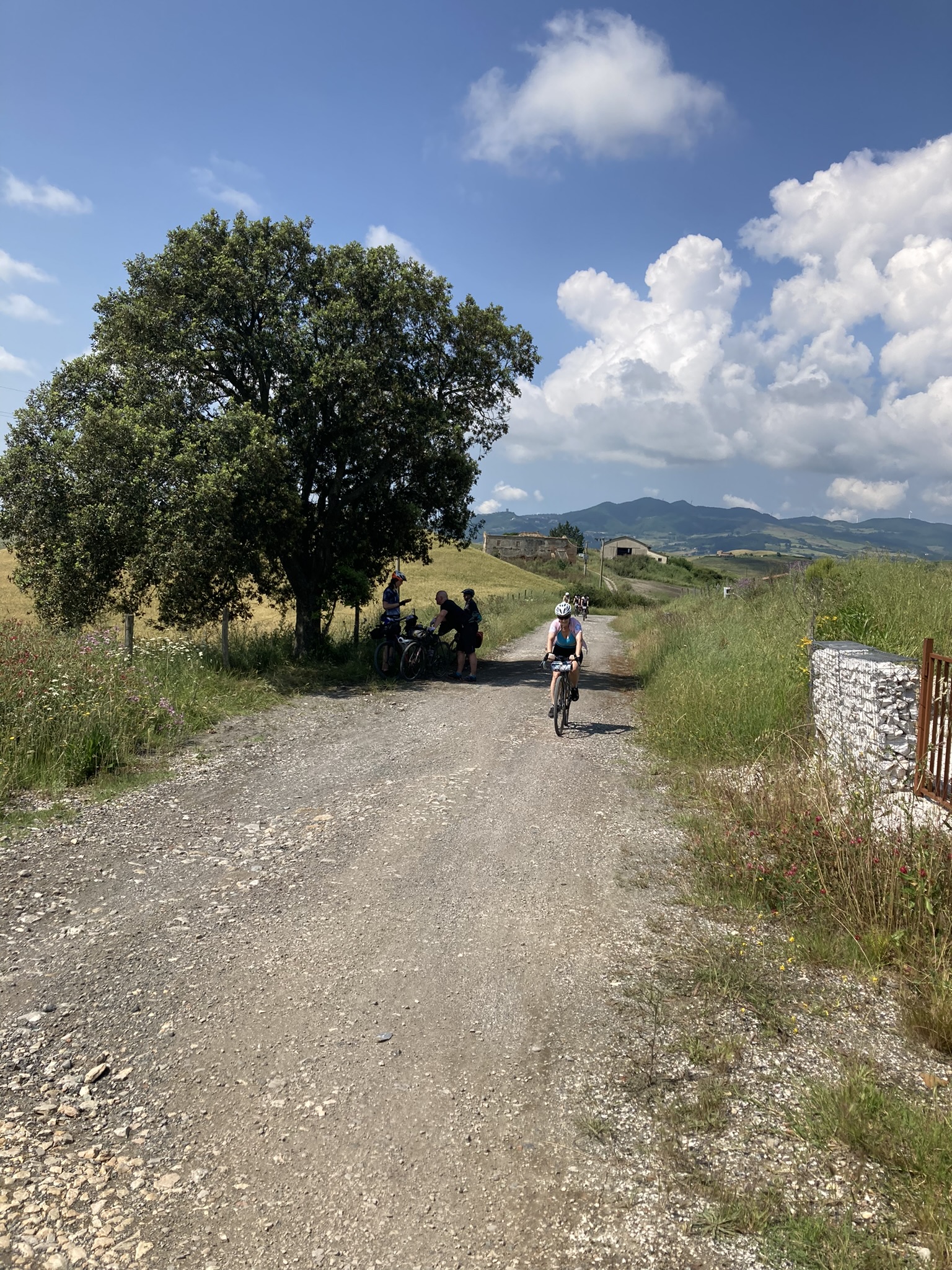 Bikepacking Italien - nahe Volterra in der Toskana: Radfahrerin auf Schotterstraße durch sanfte Hügel, mediterrane Landschaft und weiter Panoramablick.