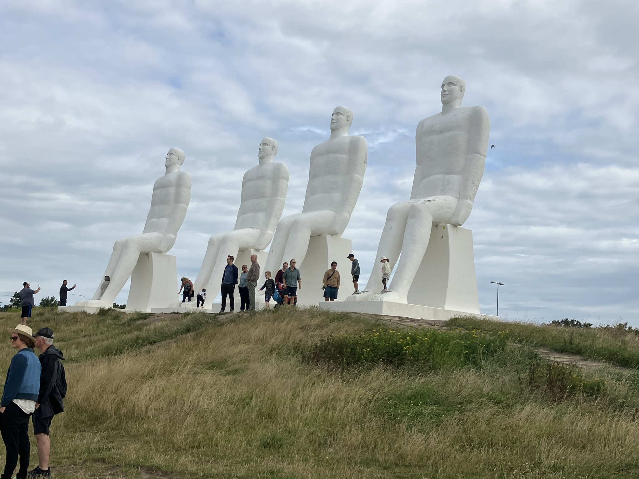 Bikepacking Dänemark - Vier große weiße Skulpturen „Mennesket ved Havet“ bei Esbjerg an der dänischen Nordseeküste mit Besuchern im Vordergrund.