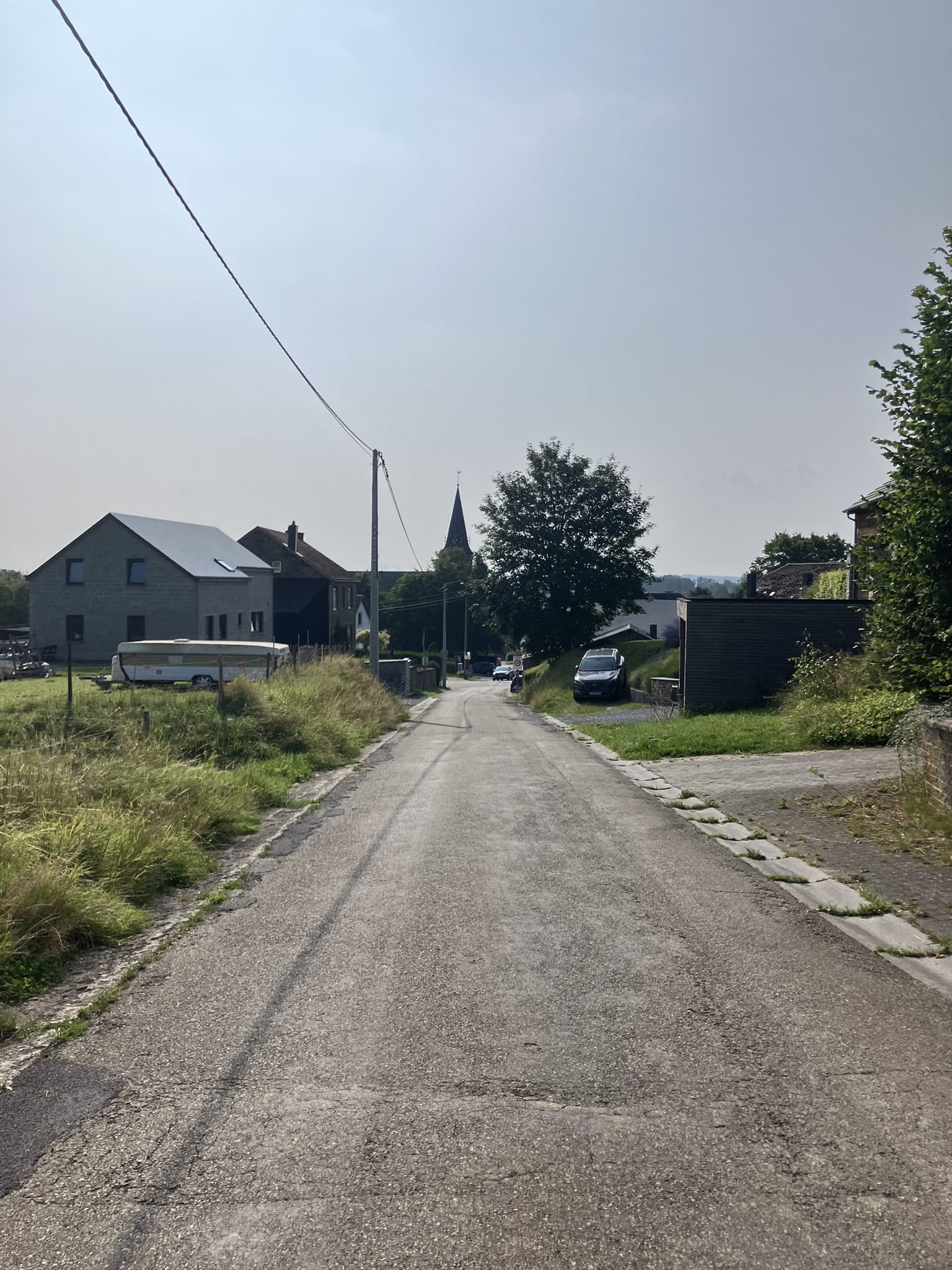 Bikepacking Belgien - Schmale Dorfstraße in Belgien mit Wohnhäusern aus Stein, Kirchturm im Hintergrund, ruhige ländliche Atmosphäre.